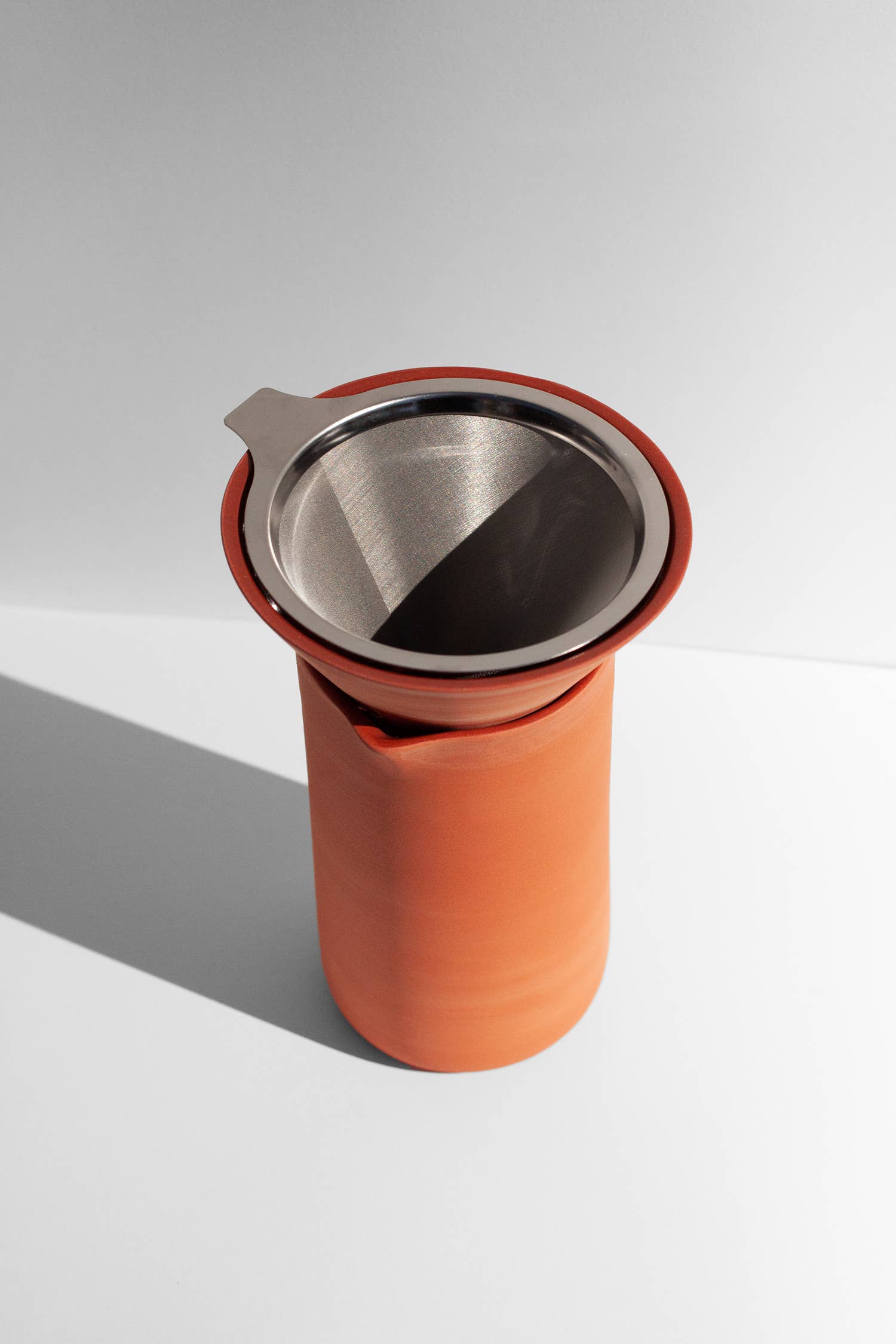 A terracotta colored coffee pour over with funnel sitting on a white surface.