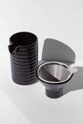 A black coffee pour over and funnel sitting on a white surface.