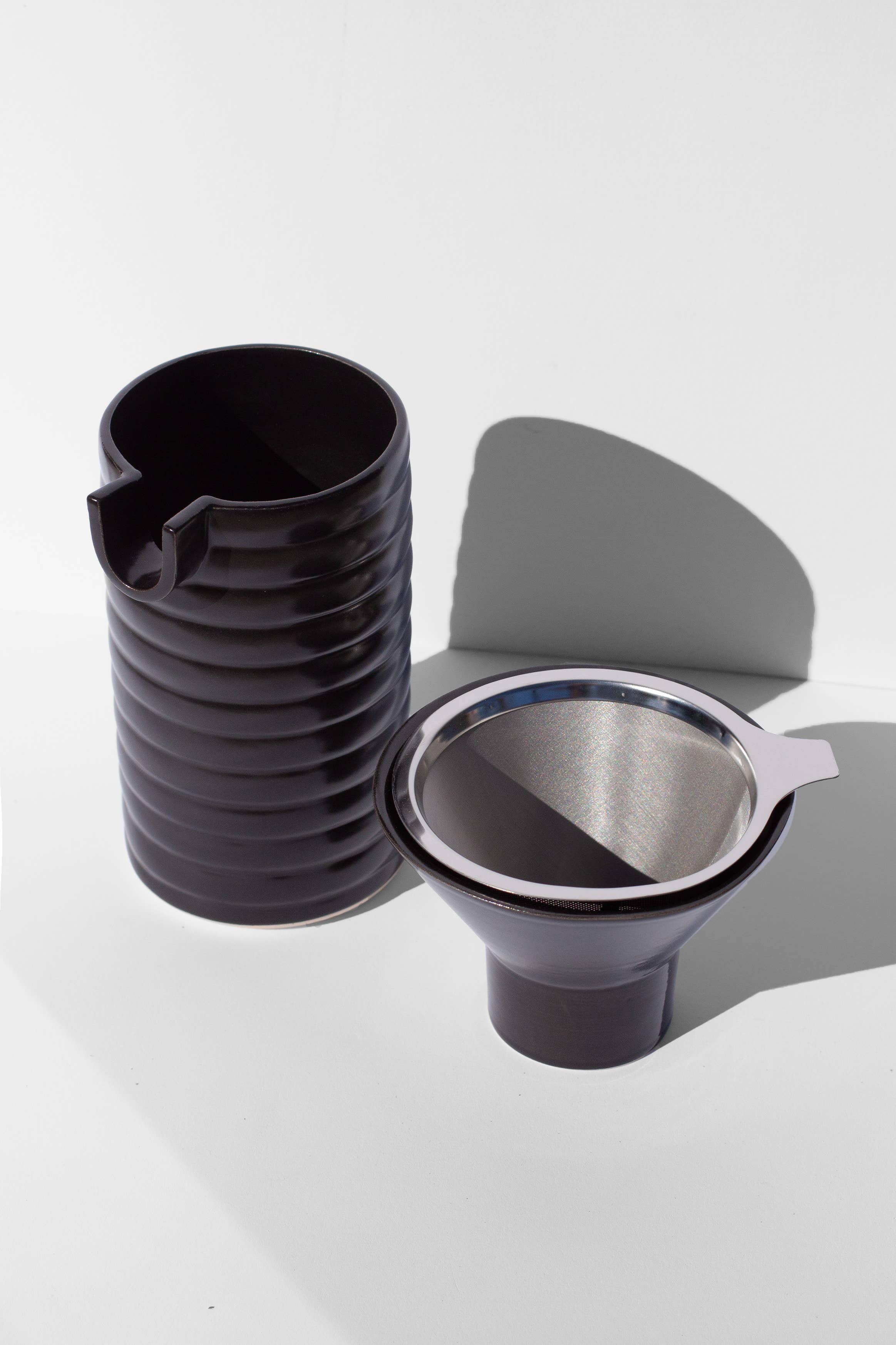 A black coffee pour over and funnel sitting on a white surface.