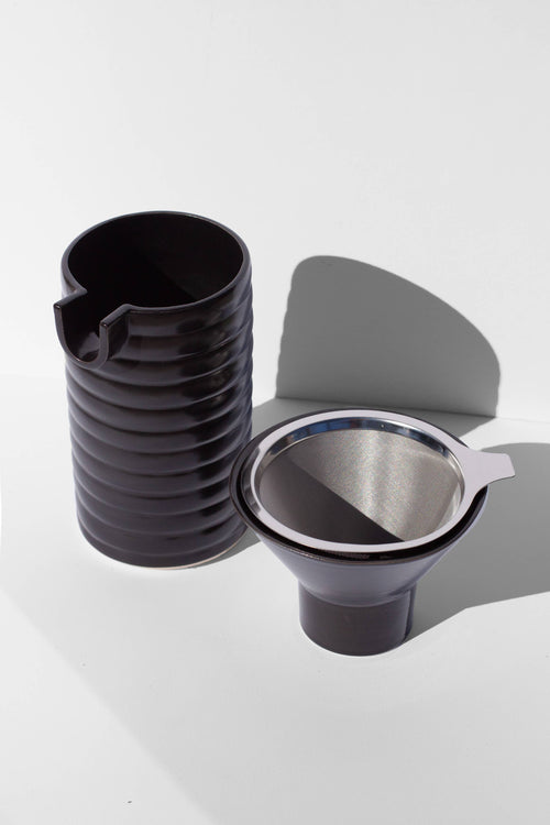 A black coffee pour over and funnel sitting on a white surface.