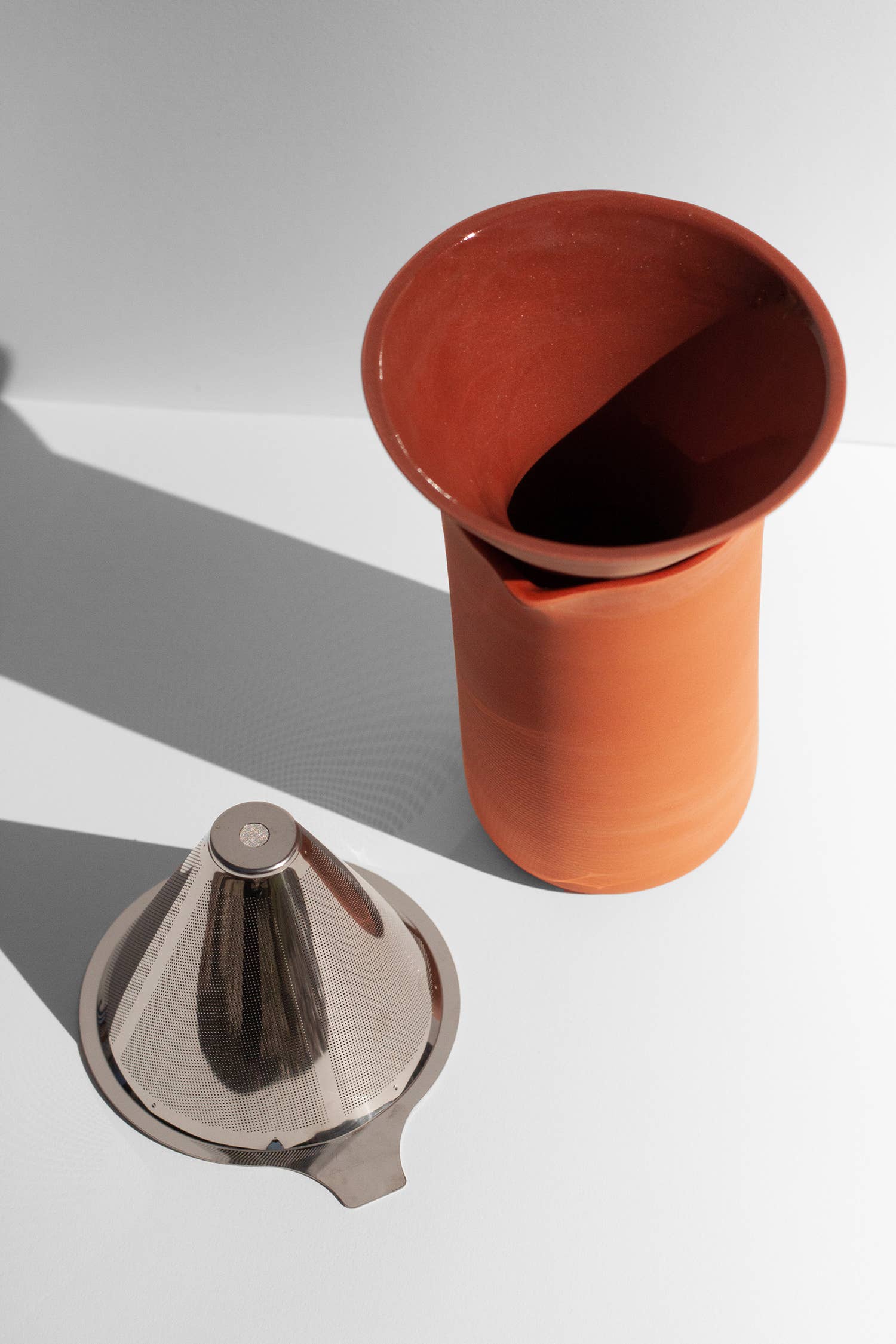 A terracotta coffee pour over with funnel and strainer sitting on a white surface.