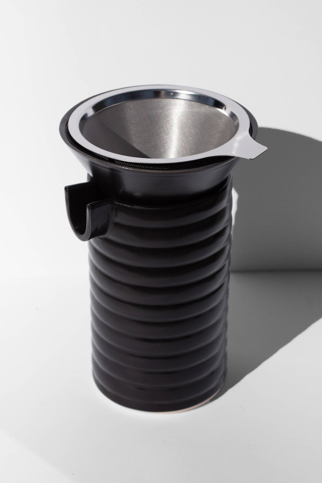 A black coffee pour over and funnel sitting on a white surface.