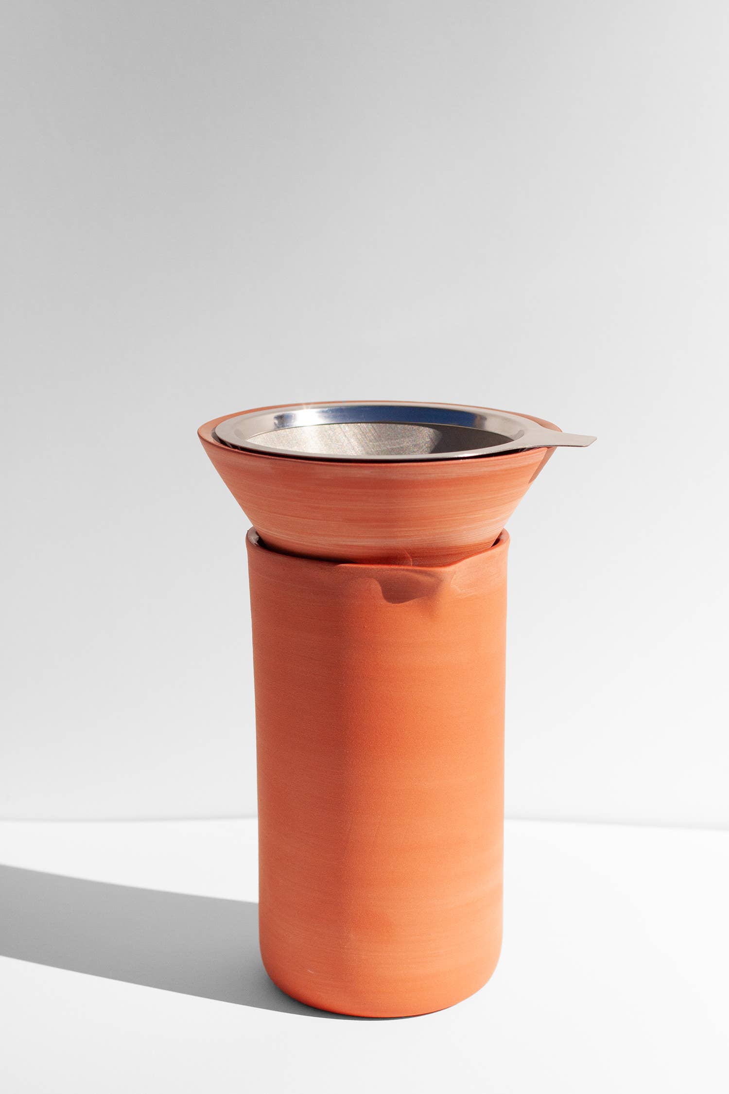 A terracotta coffee pour over and funnel siting on a white surface.