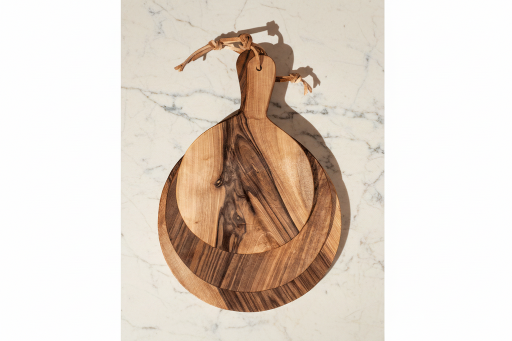 Three round Une Vie Nomade paddle style walnut cutting boards on a white marble surface.