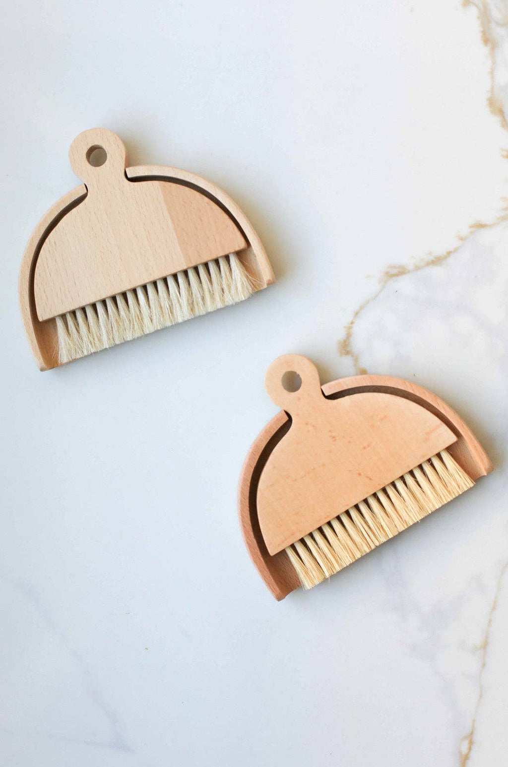 Two small cleaning brushes with bristle heads and wooden handles on a beige background