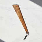 Wooden spatula with a leather strap on a light marble surface.