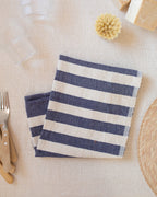 A blue and white striped kitchen towel sitting on a white surface next to utensils and plate.