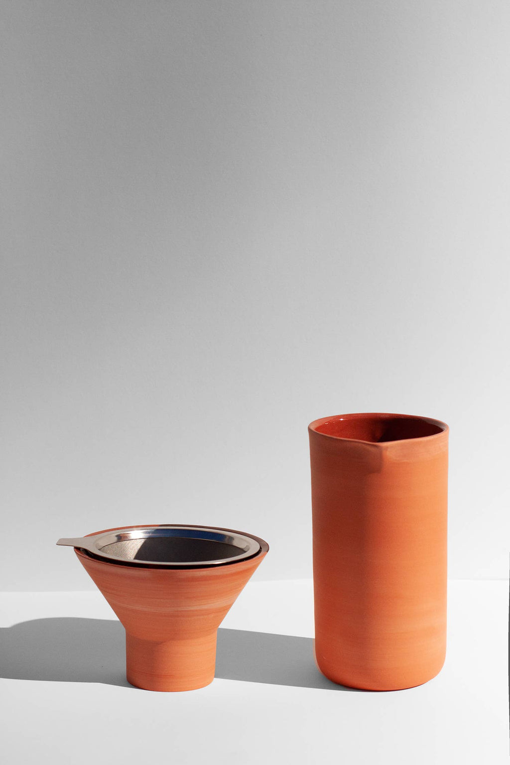 A terracotta colored coffee pour over and funnel sitting on a white surface.