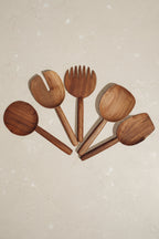 Set of 5 assorted Une Vie Nomade walnut serving spoons on a light cream colored surface.