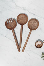 Set of three large size Une Vie Nomade walnut wooden spoons on a white countertop.