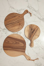 Three Une Vie Nomade round paddle shaped walnut cutting boards on a white marble surface.