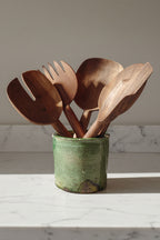 Set of five assorted Une Vie Nomade walnut spoons placed inside a green ceramic canister on top on a white marble counter.