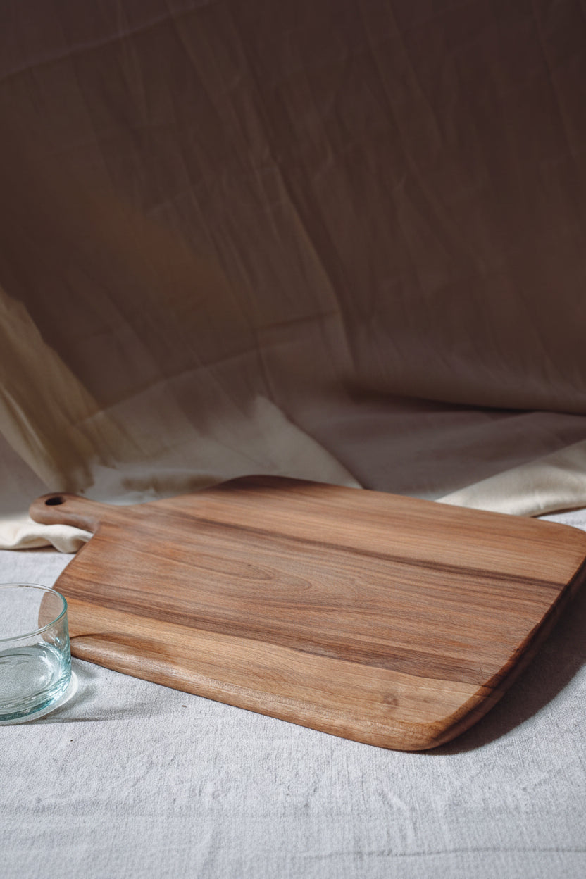 One large rectangular paddle-shaped Une Vie Nomade walnut cutting board with a neutral background.