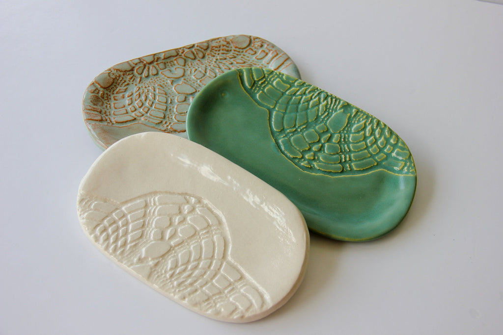 A light green, cream, and a dark green oval shaped dish being held by a person with a white background.