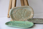 A light and a dark green, and a cream colored oval shaped dish with a white background.