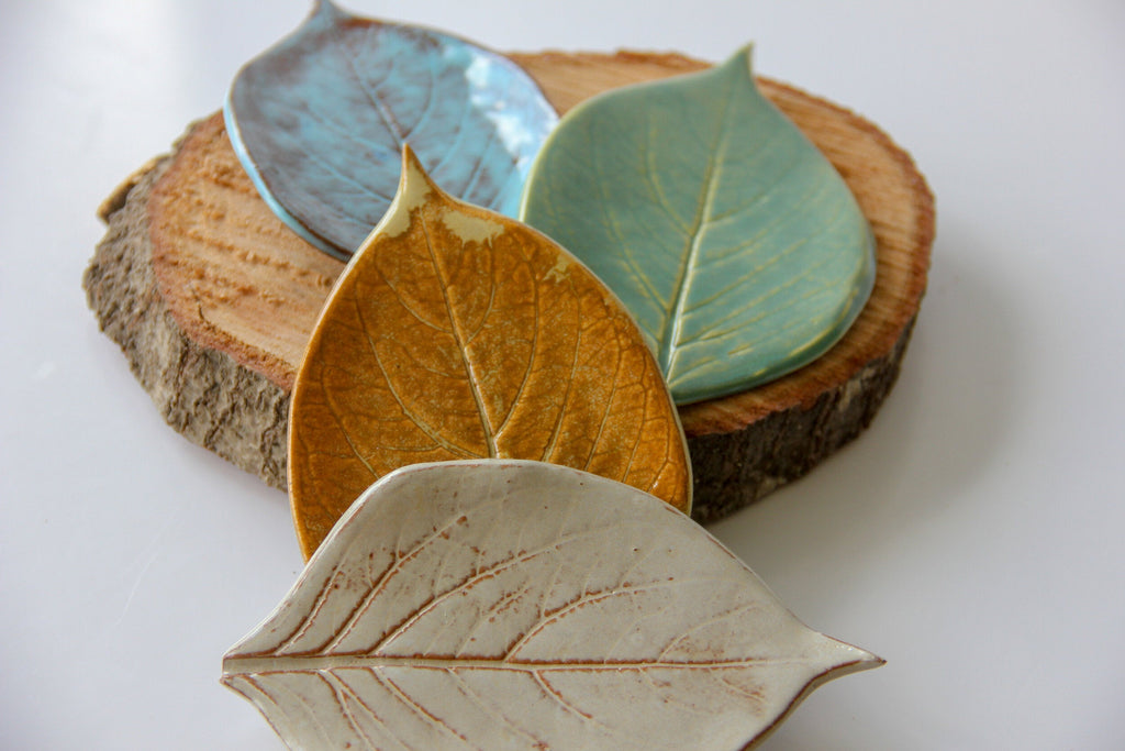 Four green plates in the shape of leaves, sitting on a round piece of wood placed on a white surface.