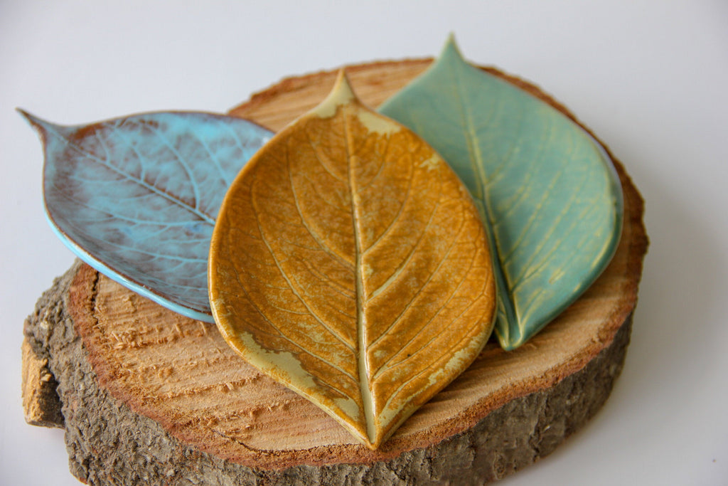Three green plates in the shape of leaves, sitting on a round piece of wood placed on a white surface.