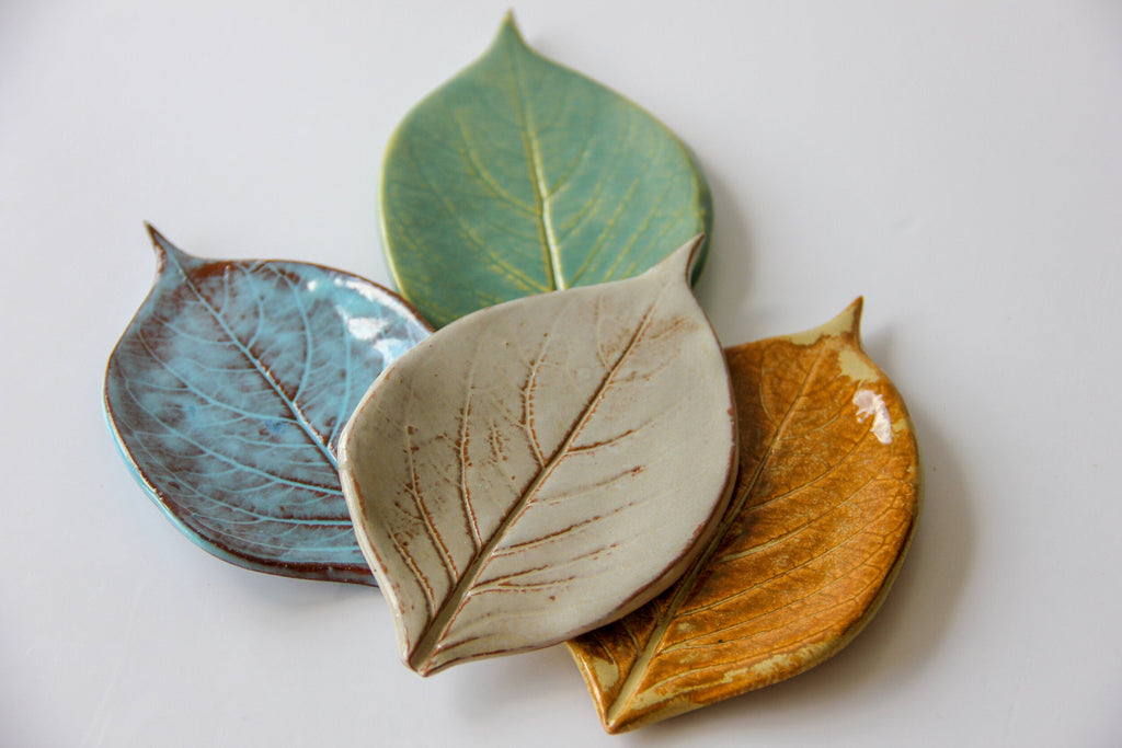 Four leaf shaped plate in different colors sitting on a white surface.