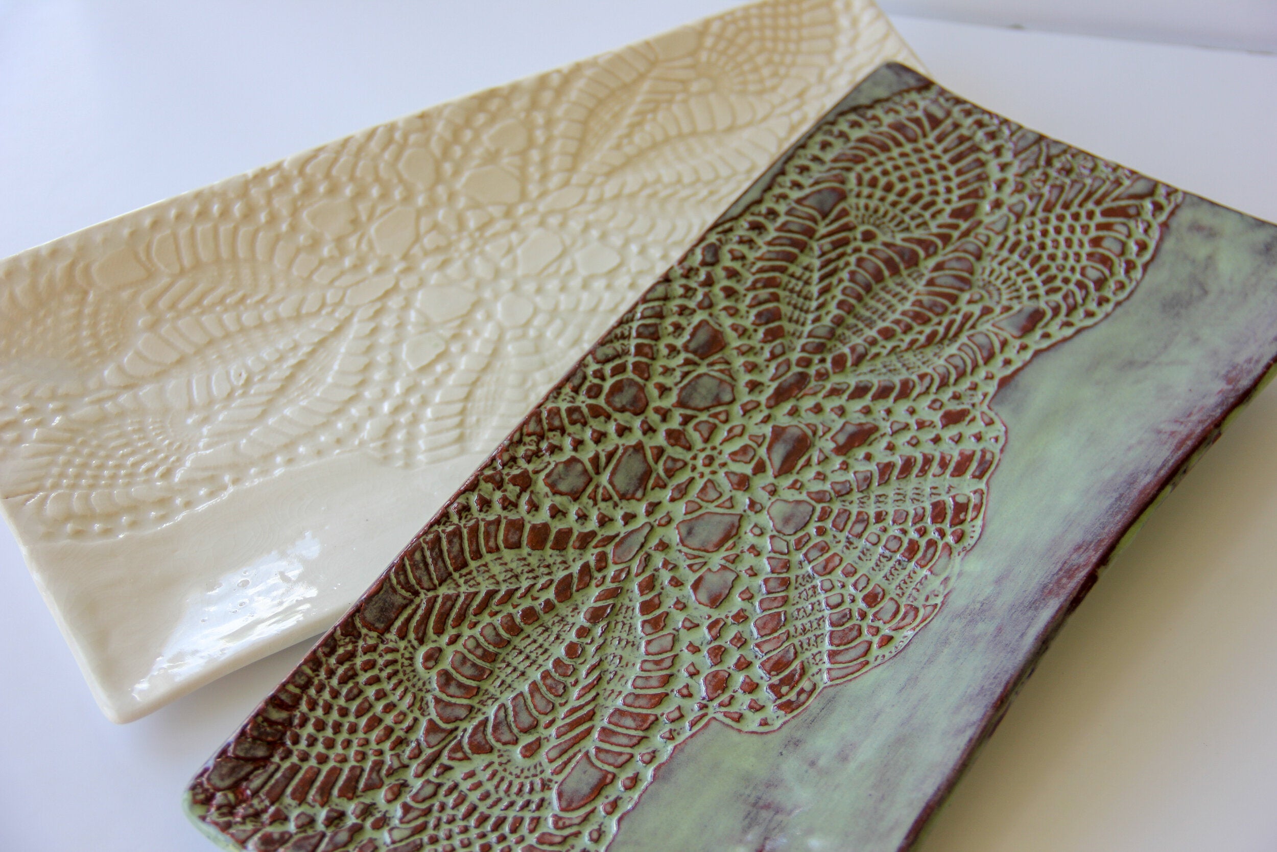 One cream rectangular platter and one green rectangular platter on a white surface.