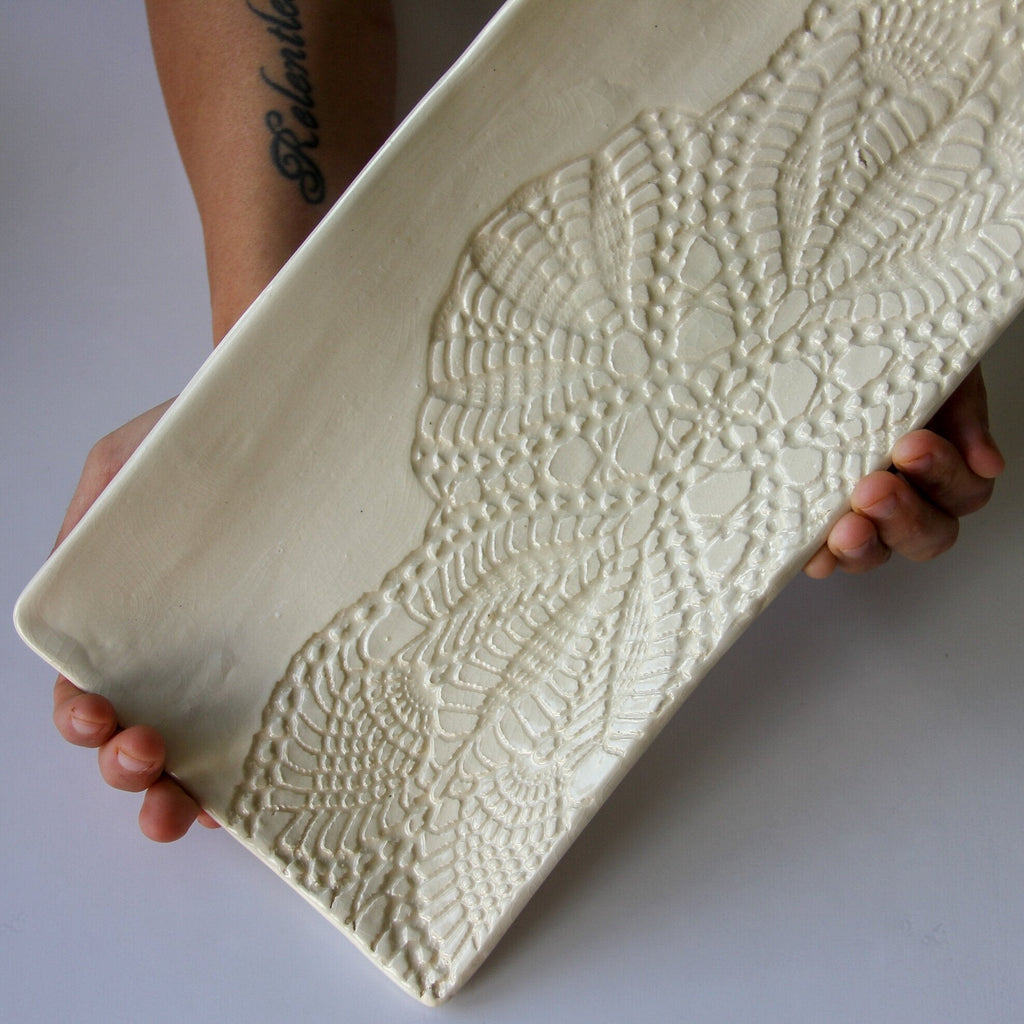 A person holding a rectangular cream colored platter with a white background.