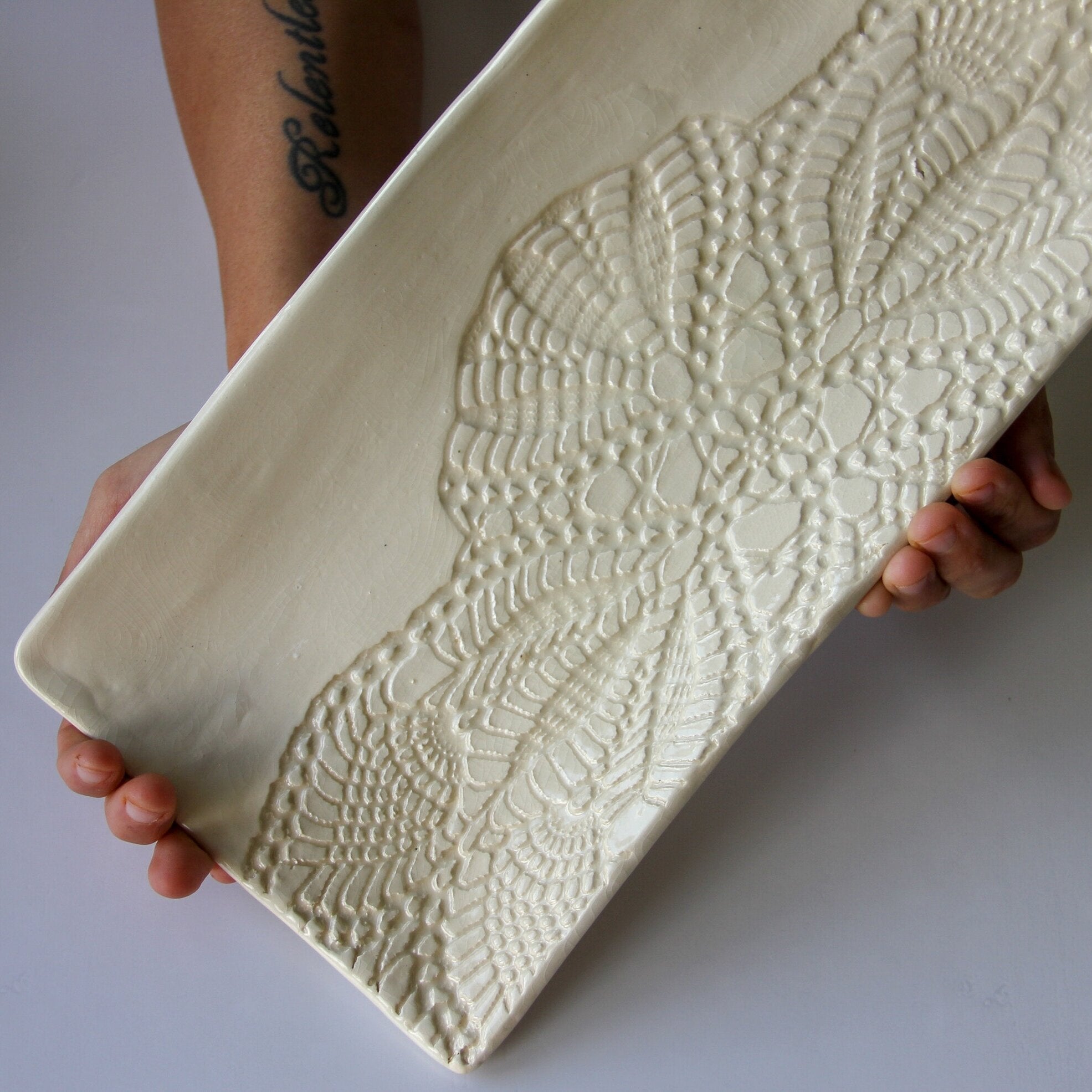 A person holding a rectangular cream colored platter with a white background.