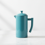 A Kuchenprofi lagoon blue French press coffee maker with a matching lid, shown on a light marble surface against a white background.