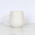 Cream colored honeycomb style coffee mug on a white background.