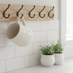 Cream colored honeycomb style coffee mug hanging on a kitchen wall rack in a white kitchen.