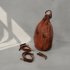 A Remington Italian Leather backpack with gold-tone hardware, shown on a gray background with detachable shoulder straps placed below it.