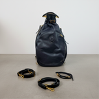 Remington black leather drawstring backpack with gold-tone hardware, shown with detachable shoulder straps on a plain gray background.