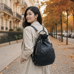 A woman wearing a beige trench coat shown from behind, wearing a Remington Black Italian leather backpack with gold hardware on a city sidewalk.