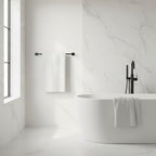 A white waffle weave bath towel hanging on a towel bar with a matching towel draped on a white bathtub.