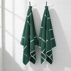two green towels with white stripe patterns hanging on hooks on a white tile wall.