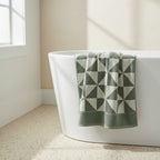sage green and white geometric patterned towel on a white bathtub.