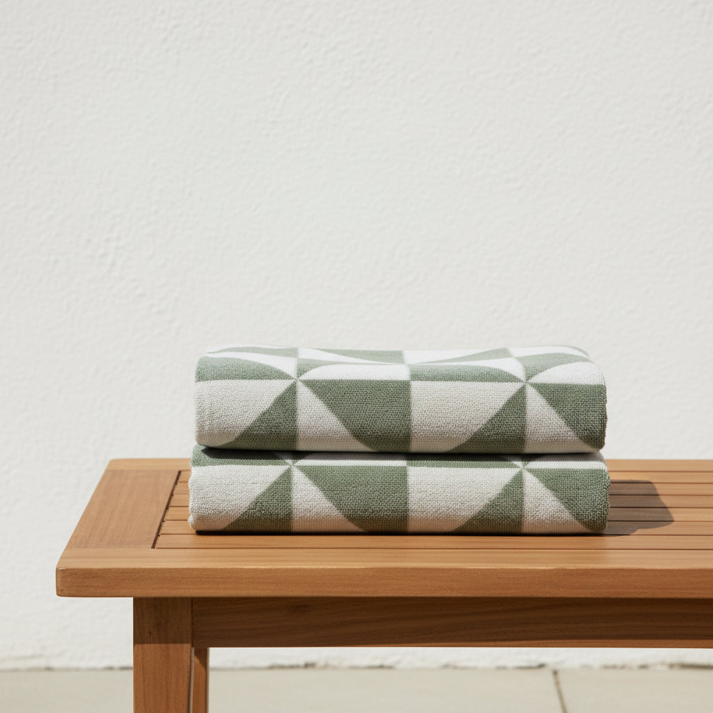 Stack of folded green and white patterned towels on top of a wood bench on a light gray background