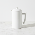 A Kuchenprofi white ceramic French press coffee maker with a lid, spout, and curved handle, set on a light marble surface against a clean white background.