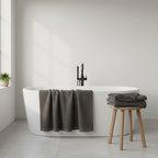 Two charcoal grey bath sheets in a white bathroom with spa tub.