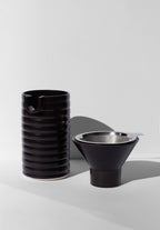 A black coffee pour over and funnel sitting on a white surface.