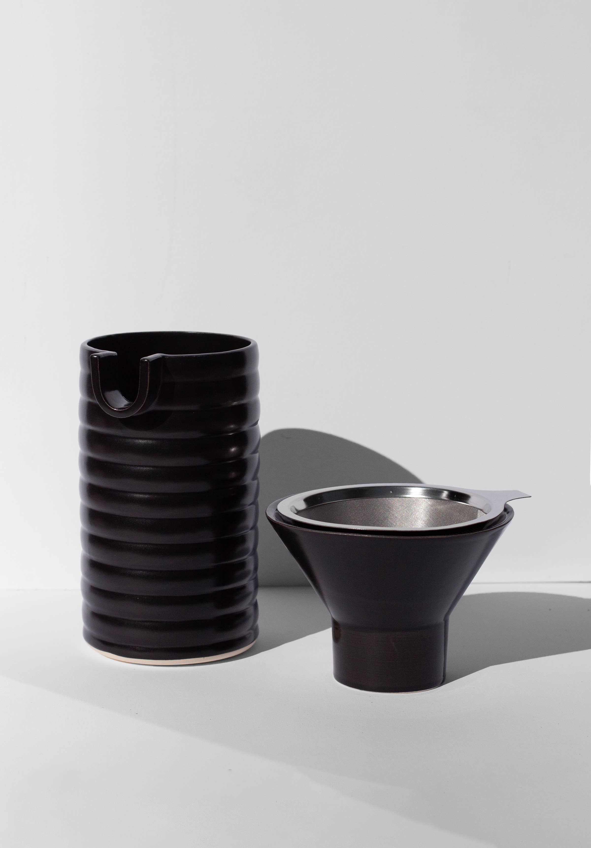 A black coffee pour over and funnel sitting on a white surface.