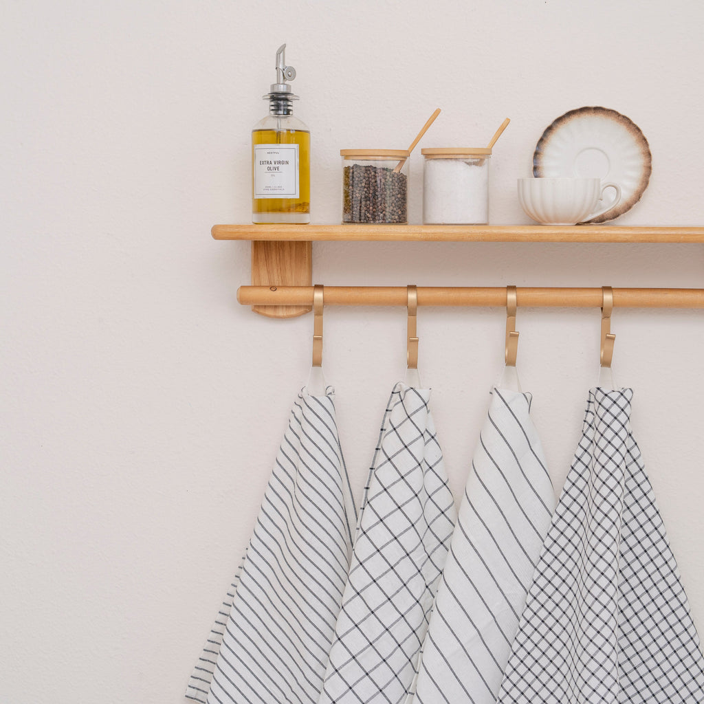 Four different white and black kitchen towels from Organic Cotton Mart hanging on hooks on a wooden rack.