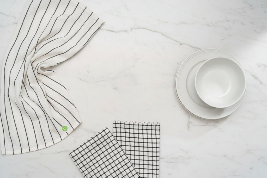 Three different white and black Organic Cotton Mart kitchen towels on a white counter.