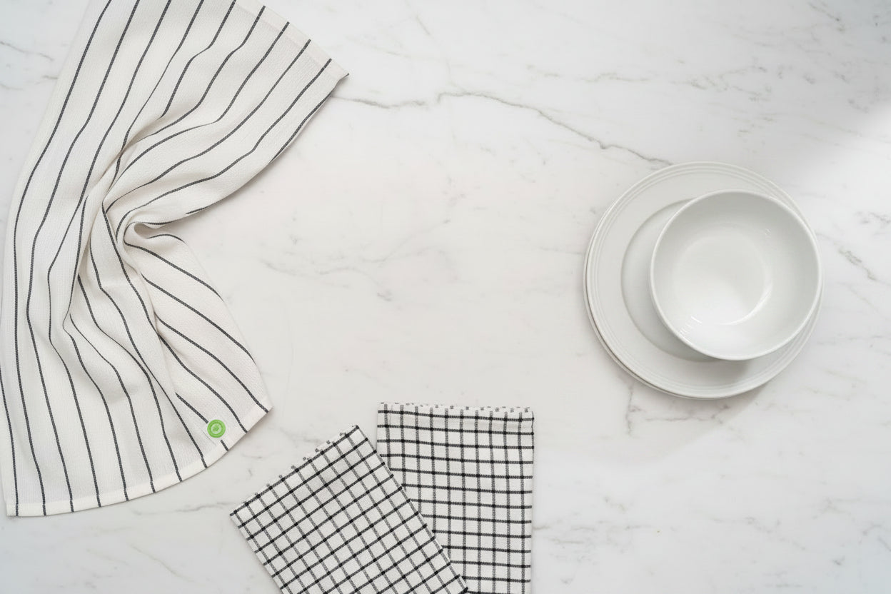 Three different white and black Organic Cotton Mart kitchen towels on a white counter.