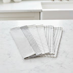 Six white and black kitchen towels from Organic Cotton Mart on a white kitchen background.