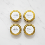 4-Pack tin candle set with grapefruit & spearmint, lemongrass & tangerine, Hello Sunshine, Rosemary & lemon scented candles on a light surface.