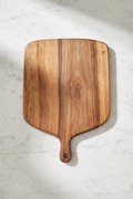 Large wide rectangular paddle-shaped Une Vie Nomade walnut cutting board on a white marble surface.