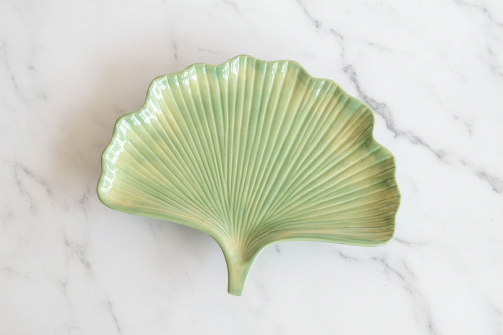 Green ginkgo plate on w white marble surface.